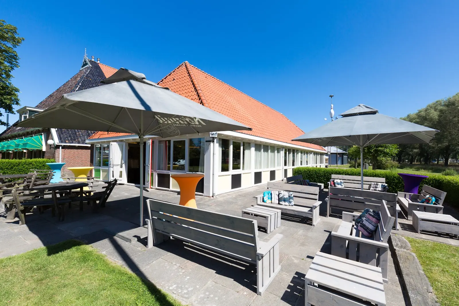 Het terras van De Stolp met parasols en houten banken in de zon